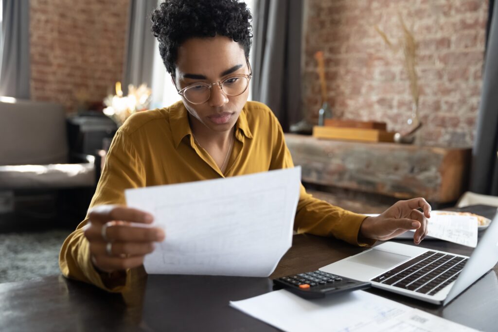 young adult looking over paperwork at a table with her laptop open