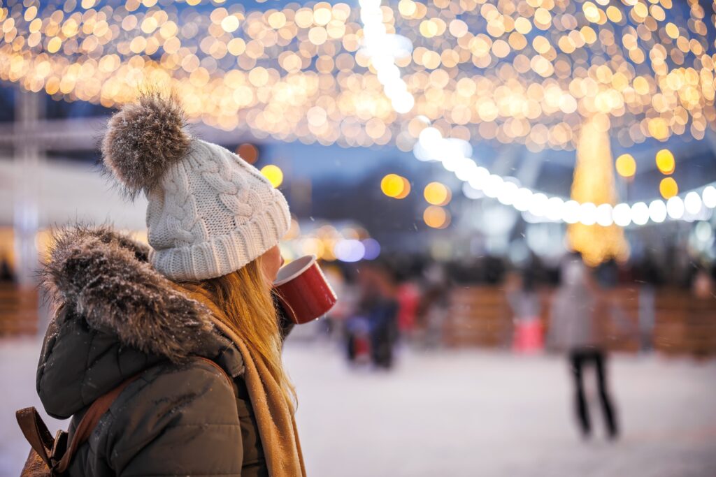 Woman drinking hot chocolate during a winter festival watching ice skating under Christmas lights
