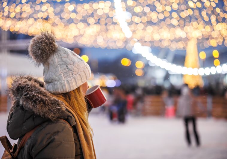 Woman drinking hot chocolate during a winter festival watching ice skating under Christmas lights